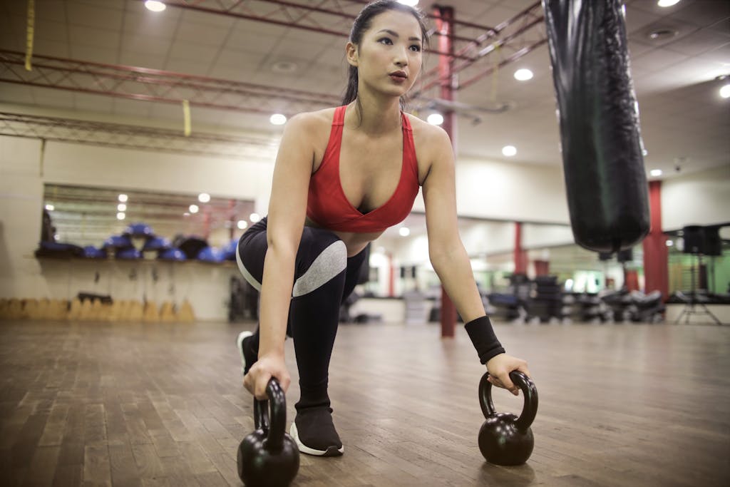 female athlete in sportswear squatting with kettlebells 