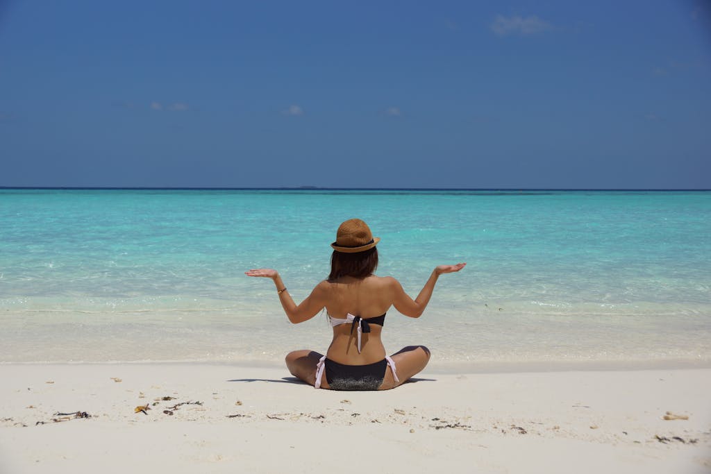 Woman in Black and White Bikini Sitting on White Stand Facing Beach during Daytime