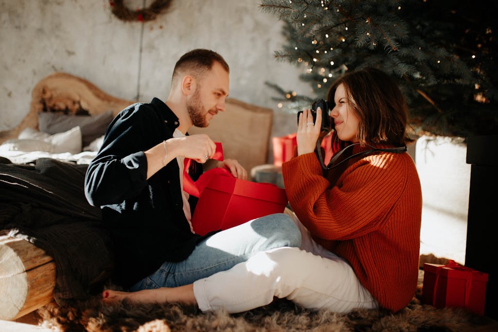 A joyful couple exchanges gifts under the Christmas tree indoors.
