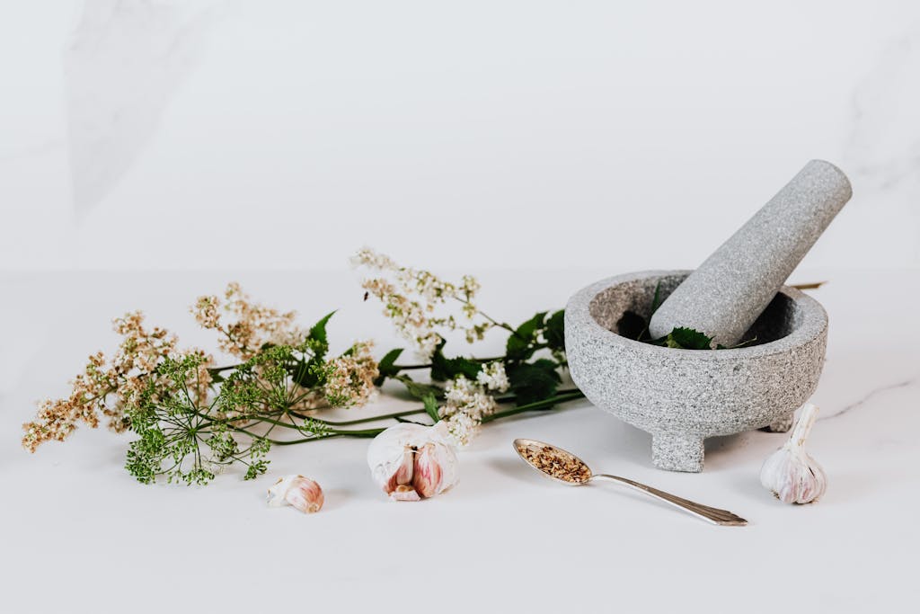 A minimalist setup featuring a stone mortar and pestle with garlic and herbs on a neutral background.