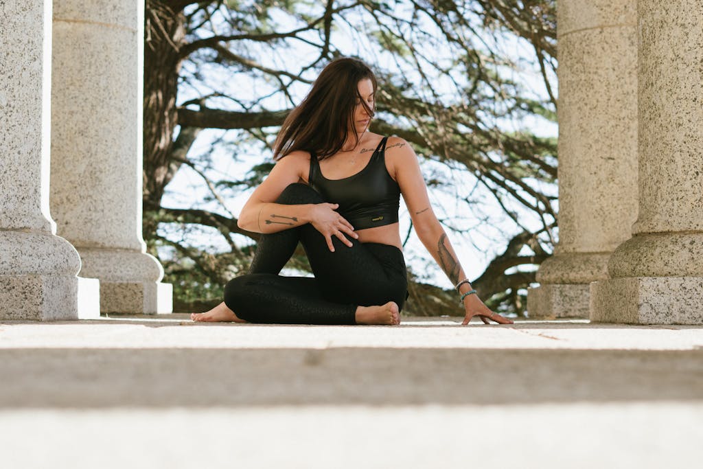 A woman in black sportswear meditates in a serene outdoor setting, surrounded by nature.