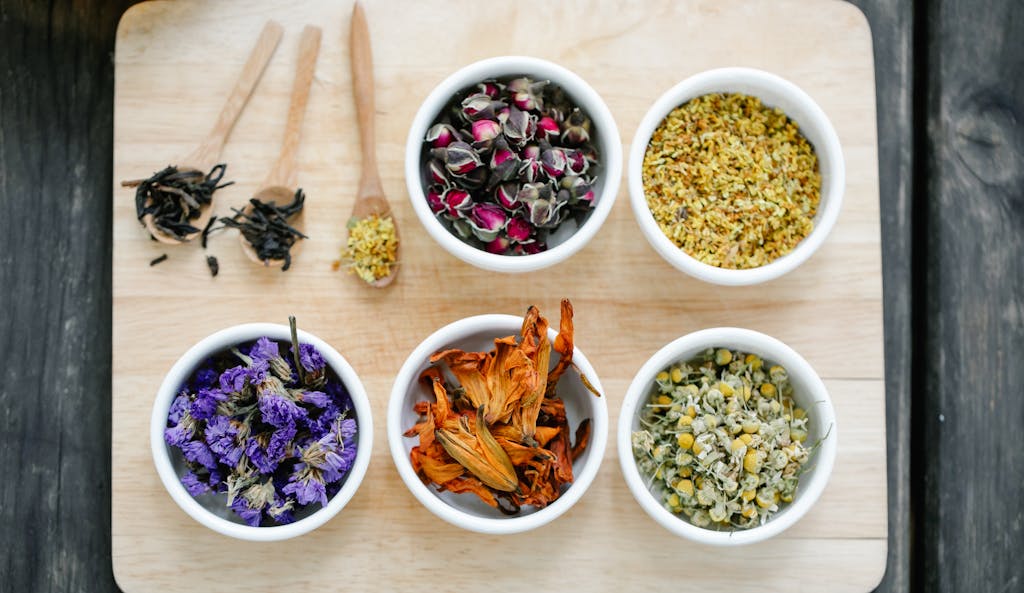Colorful dried flowers and herbs displayed in bowls on a wooden board.