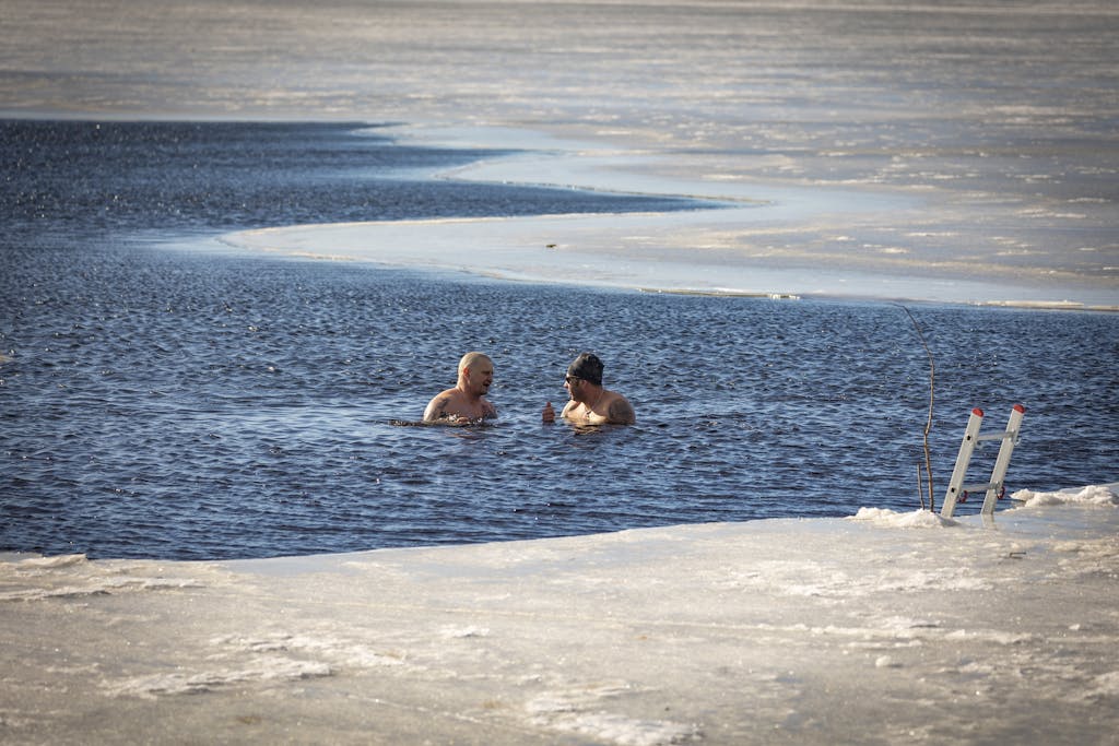 Two men brave the cold for a swim in a partially frozen lake during winter.